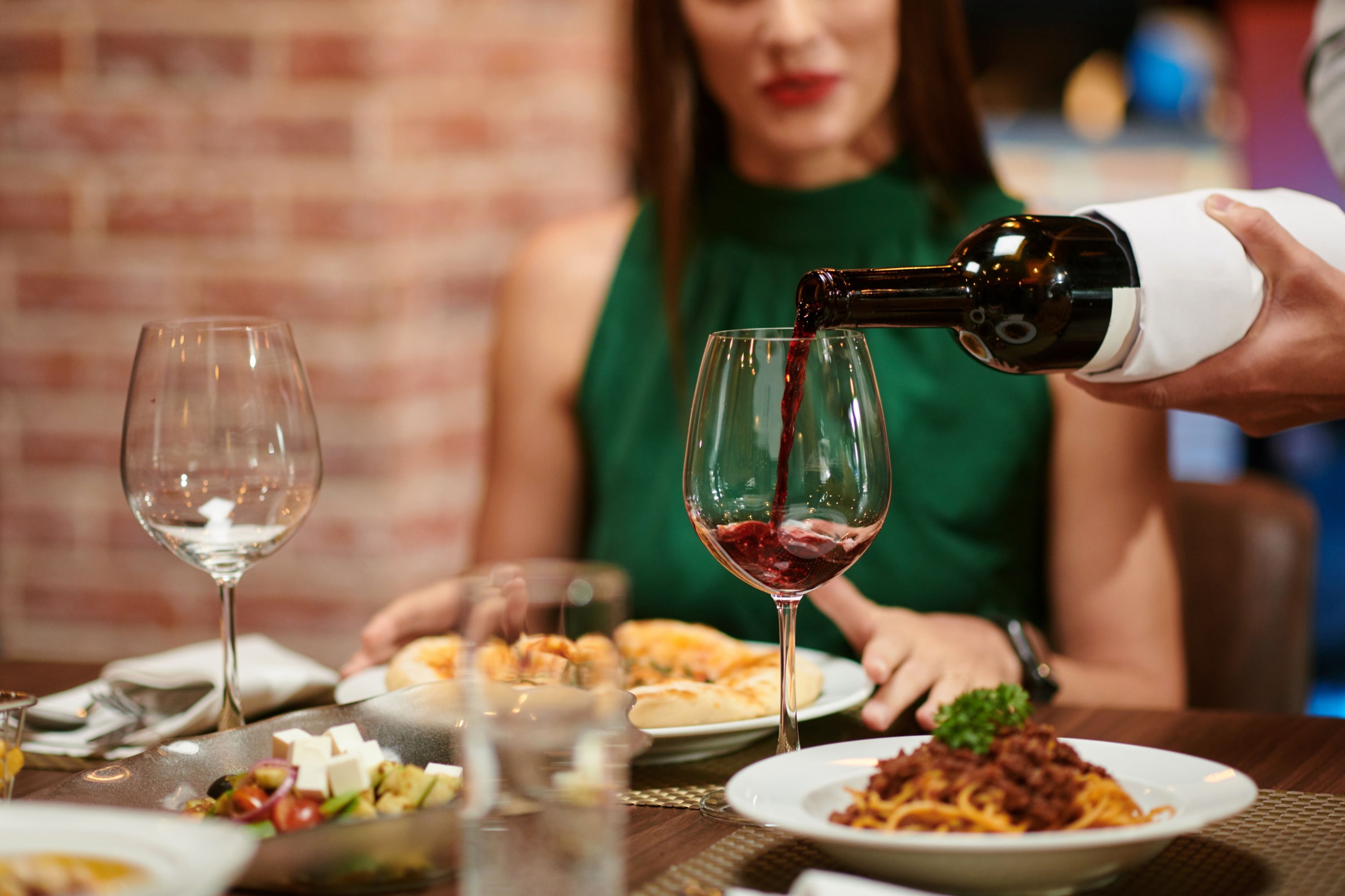 Waiter filling wine glass for yuong elegant woman sitting at restaurant